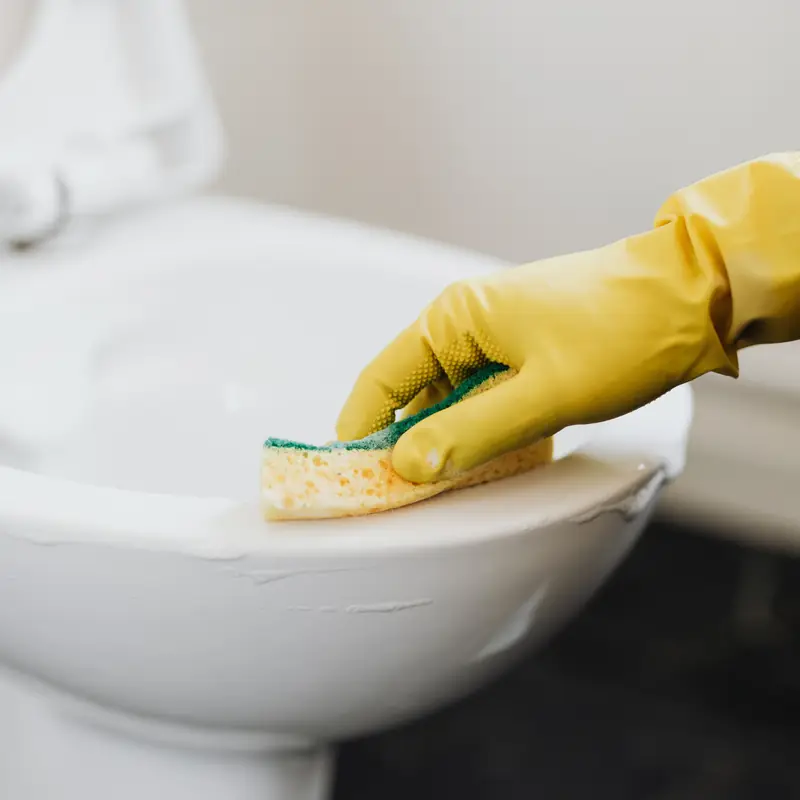 Close-up of a toilet being scrubbed with a sponge during detailed bathroom cleaning