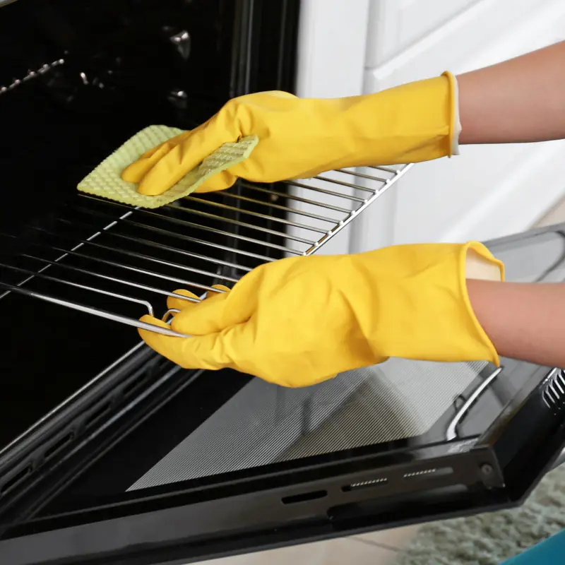 Gloved hands wiping an oven rack during a kitchen cleaning
